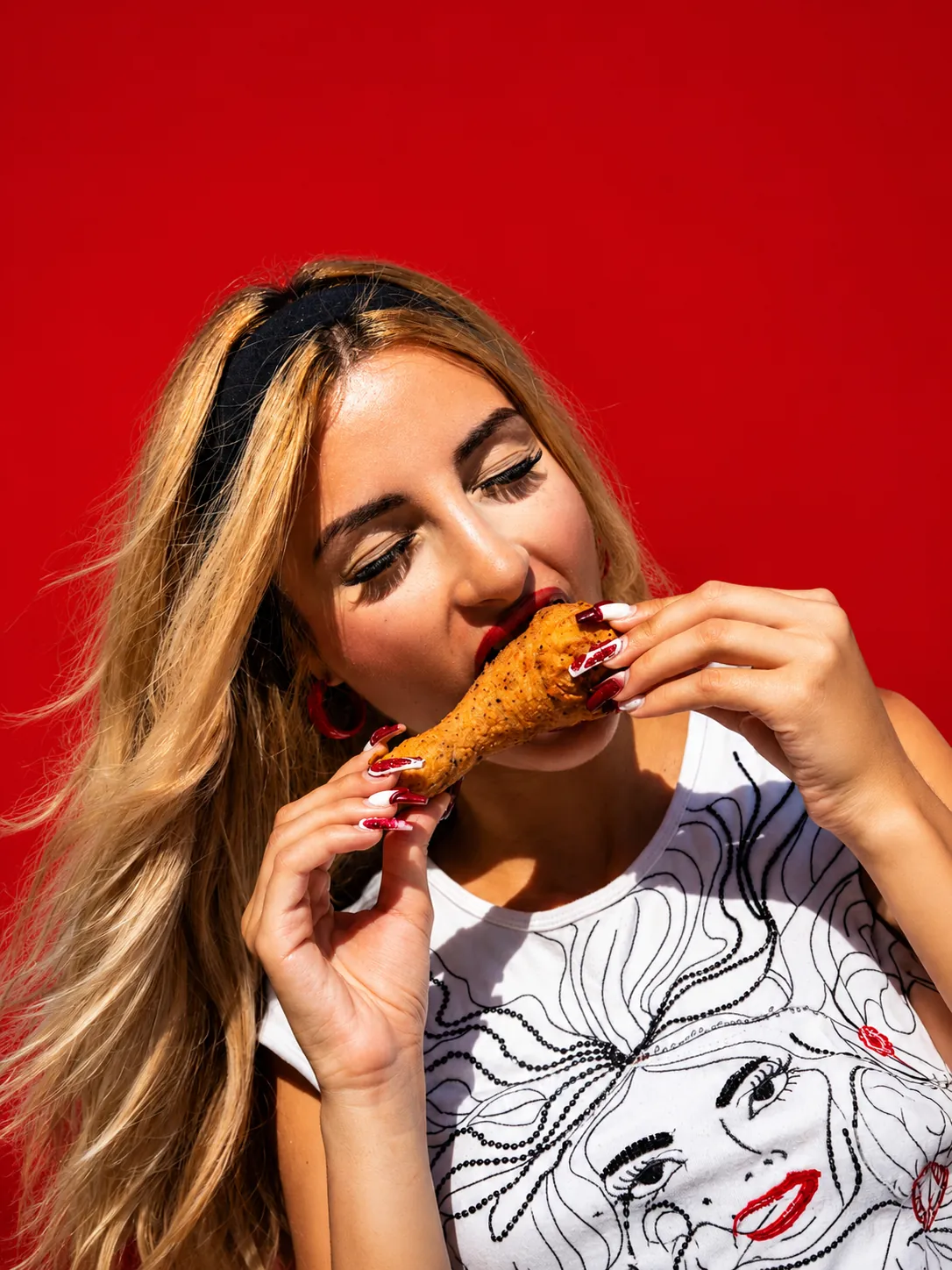Woman biting into CFC fried chicken against a red background